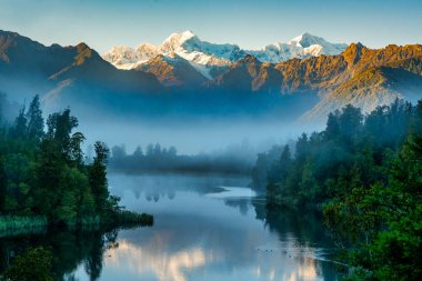 Mist at dawn  preventing the reflections of the snow capped southern alps on the calm water at Lake Matheson clipart