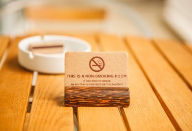 A non-smoking room warning sign on coconut rest with a white ceramic ashtray and match on a wooden table in a hotel balcony telling guests to smoke outside the hotel room clipart