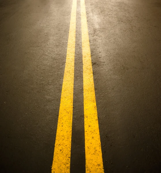 A shiny surface of a asphalt road with double middle yellow lines which tell car drivers not to overtake to avoid accident because in some areas it is dangerous and violate traffic rule and regulation