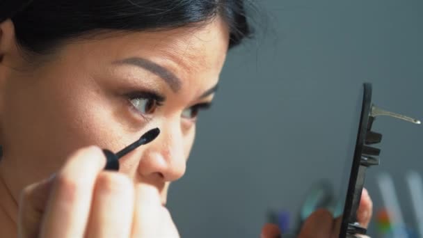 Kvinna målar sina nedre ögonfransar med mascara. Hon håller en spegel i ena handen och sminkar sig med den andra handen. Tillämpa make-up konceptet. Högkvalitativ 4k-film — Stockvideo