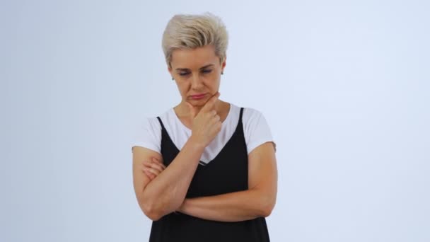 Adult woman on white background looks thoughtfully and ponders. She holds her chin in her hand and nods approvingly. Blonde model with short hair. — Stock Video