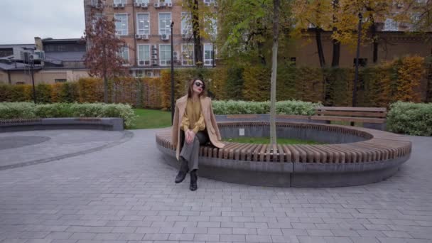 Sensueel jong meisje zit in het park tegen de achtergrond van de herfststad te wachten op een date of hun vriendinnen. Hoge kwaliteit 4k resolutie beeldmateriaal — Stockvideo