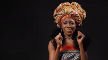 Geleneksel başlık güzel Afro-Amerikan kadın dans ediyor ve siyah arka planda tek başına kameraya bakıyor. Yüksek kaliteli 4k çözünürlük görüntüleri