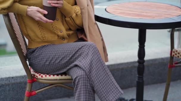 Close up câmera deslizar para cima de jovem bonita francesa olhando menina em uma boina vermelha bebe café quente ou chá sentado no terraço de um restaurante ou café na cidade urbana de outono. 4K UHD — Vídeo de Stock