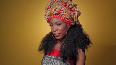 Geleneksel başlık takmış kamera karşısında göz kırpıyor sarı arka planda izole edilmiş güzel Afro-Amerikan genç bir kadın. Yüksek kaliteli 4k çözünürlük görüntüleri