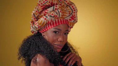 Nazikçe dokunarak güzel kıvırcık saçlı güzel Afro-Amerikan kadın milli başlık takmış sarı arka planda yanlamasına kameraya bakıyor. Yüksek kaliteli 4k çözünürlük görüntüleri