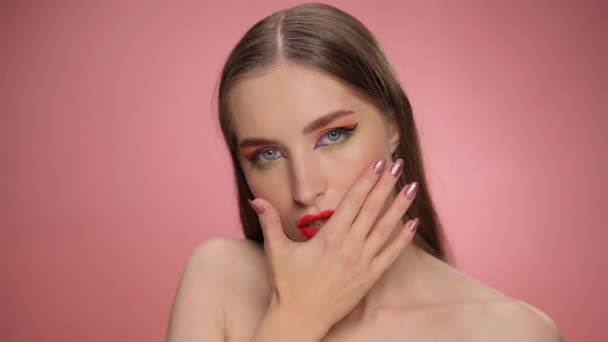 Una hermosa modelo con lápiz labial rojo en sus labios mira a la cámara y con su mano mancha el lápiz labial de sus labios, convirtiendo la belleza en maquillaje de desorden. Imágenes de FHD — Vídeo de stock