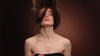 Güzel manken başını kaldırıyor, uzun ve sağlıklı saçlarını havada sallıyor ve siyah arka planda izole edilmiş kameraya gülümsüyor. Yüksek kaliteli FullHD görüntüler