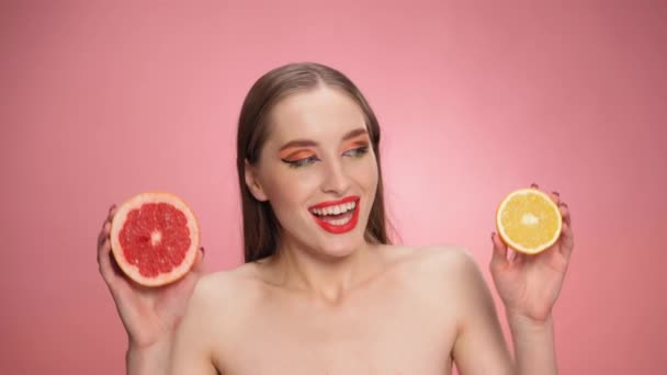 O femeie tânără frumoasă, cu fructe suculente de portocale și grapefruit în mâini, zâmbetul se uită la camera izolată pe fundal negru. Cosmetice naturale. Imagini FHD — Videoclip de stoc