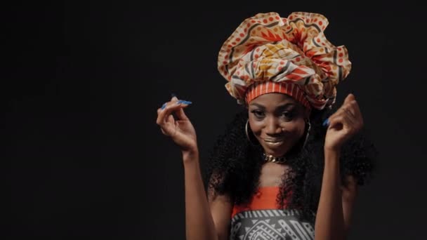 Φορώντας παραδοσιακή φορεσιά Αφρο-Αμερικανίδα νεαρή γυναίκα χορεύει χειροκροτώντας και χαμογελώντας κοιτάζοντας την κάμερα απομονωμένη σε μαύρο φόντο. Υψηλής ποιότητας 4k βίντεο ανάλυσης — Αρχείο Βίντεο