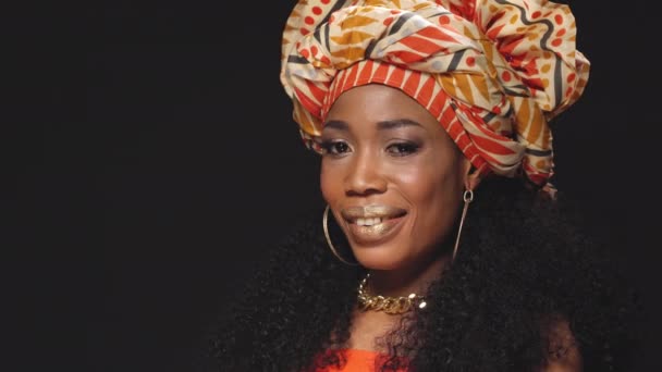 Winking wearing traditional headdress beautiful Afro American young woman looking at camera sideways isolated on black background. High quality 4k resolution footage — Stock Video