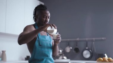Seksi Afrikalı bardağı şişeden sütle dolduruyor ve mutfakta dikilip kameraya poz veriyor. Yüksek kaliteli görüntüler