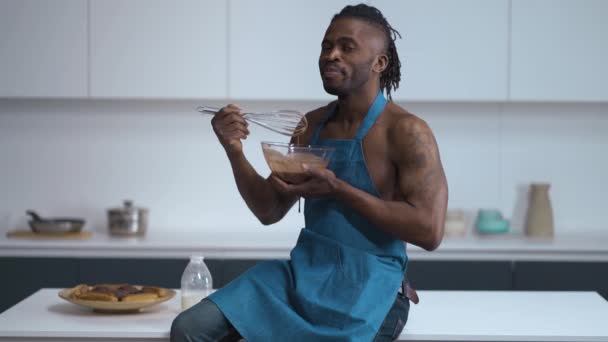 Sexy man. Handsome African on kitchen in blue cover-slut. Cook lick a Choco cream from wire whisk. — Stok video