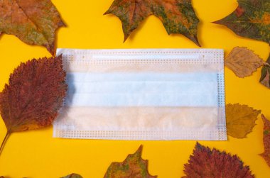 Sonbahar yapraklarının yaratıcı bileşimi ve sarı arka planda tıbbi bir maske. İkinci dalga koronavirüs enfeksiyonu. Kartpostal Üst görünüm, reklam metni için alan