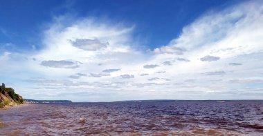 Volga Rive, Rusya. Kumsal uzakta. Nehrin kıyısında, ağaçlarla kaplı. Kıyının bir kısmı taştan. Açık, güneşli bir gün, bulutlu mavi bir gökyüzü. Uzayı kopyala Şehir simgesi. Manzara. Düzgünce