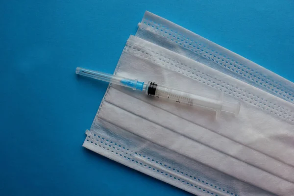 Eine Spritze mit Nadel liegt auf einer medizinischen Maske auf blauem Grund. Impfen. Coronavirus. Das Konzept der Medizin und Immunität. Impfungen gegen Virusinfektionen. Flach. Kopierraum — Stockfoto