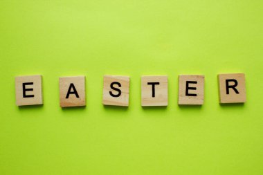 Paskalya, alfabenin tahta harflerindeki kelime. Sarı arka planda izole edilmiş. Paskalya ziyafeti. Harfler ortalanmış.