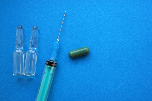 Syringe with needle, vials with medicine, tablets lie on blue background. Vaccination. Coronavirus. The concept of medicine and immunity. Vaccination against viral infections. Copy the space. Flatly