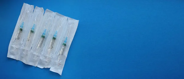 Syringes with a needle in the package lie on a blue background. Vaccination. The concept of medicine and immunity. Vaccination against viral infections. Copy space. Flatly. Banner.