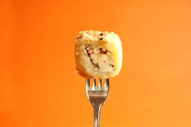 Ortadaki çatalda taze suşi rulosu, turuncu arka planda yalıtılmış. Sopasız suşi nasıl yenir? Asya yemekleri. Uzayı kopyala Yakın plan.