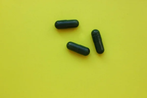 Yeşil tabletler sarı arka planda yatıyor. Sağlık ekibi. Uyuşturucu kullanımı. Tedavi. Evde ilk yardım çantası. Hastalık. Antibiyotikler. Metin için boşluk kopyalanıyor. Yukarıdan görüntüle