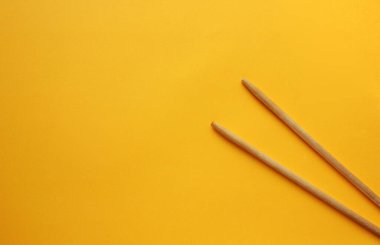 Sarı arka plandaki tahta çubukların üzerinden manzarayı seyret. Çubuklar sağ tarafta. Yiyecek aletleri. Düz yatıyordu. Boşluğu kopyala.
