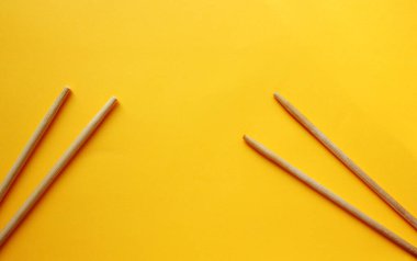 Sarı arka plandaki tahta çubukların üzerinden manzarayı seyret. İki çubuk farklı tarafta. Yiyecek aletleri. Düz yatıyordu. Boşluğu kopyala.