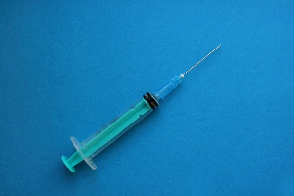 Eine Spritze mit Nadel ruht auf blauem Grund. Impfung, Injektion, Injektion, Behandlung, Antibiotikum, nakrotisch. Das Konzept der Medizin und Immunität. Flach. Kopierraum — Stockfoto