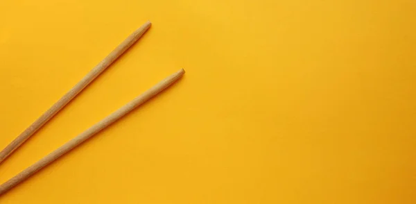 View from above on wooden chopsticks on a yellow background. Sticks are on the left side. Food appliances. Flat lay. Copy space. banner — Stock Photo, Image