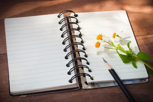 Notebook with black pencil, white flowers on wooden table