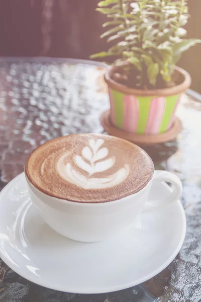 Närbild av vit kopp med varm latte art på glasbord — Stockfoto