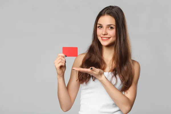 Lachende vrouw leeg creditcard in wit t-shirt tonen, geïsoleerd over grijze achtergrond — Stockfoto