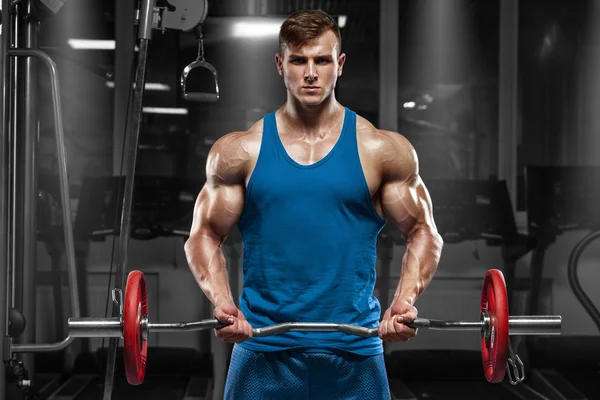 Muscular man working out in gym doing exercises with barbell at biceps, strong male