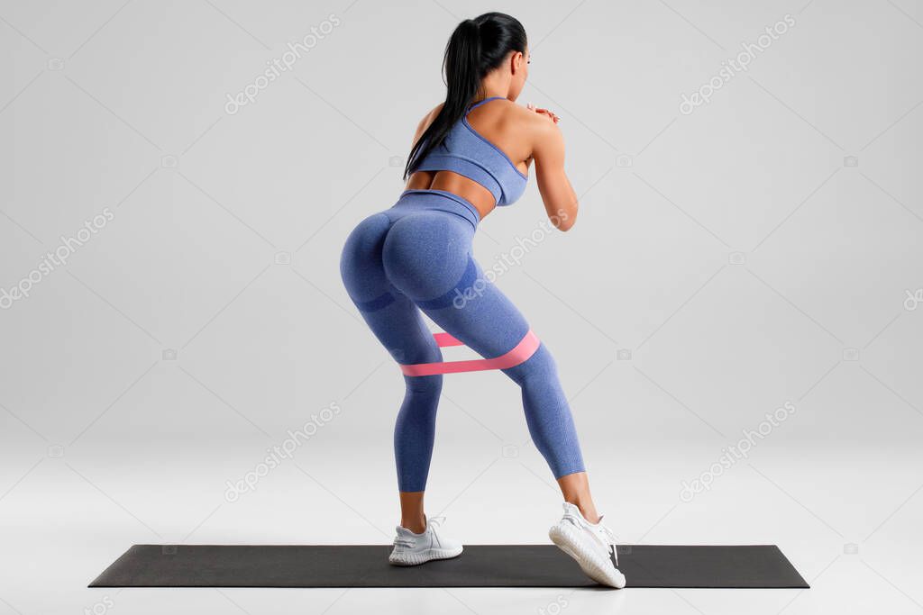 Fitness woman doing exercise for glute with resistance band on gray background. Athletic girl working out