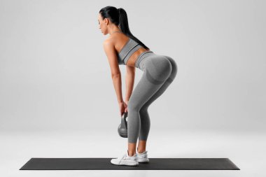 Atletik kız gri arka planda kalça kasları için kaldırma egzersizi yapıyor. Spor salonundaki kadın kettlebell ile çalışıyor.