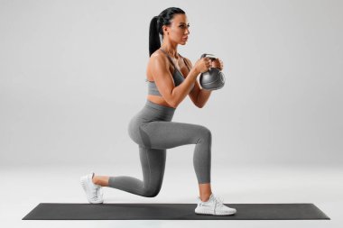 Aktif bir kız kettlebell ile hareketli egzersizler yapıyor, bacak kası eğitimi alıyor. Fitness kadını öne doğru bir adım öne atarak atlıyor.