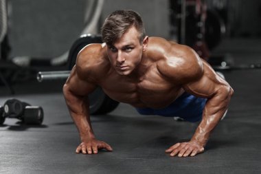 Spor salonunda şınav çeken kaslı bir adam. Güçlü bir erkek antrenman yapıyor.