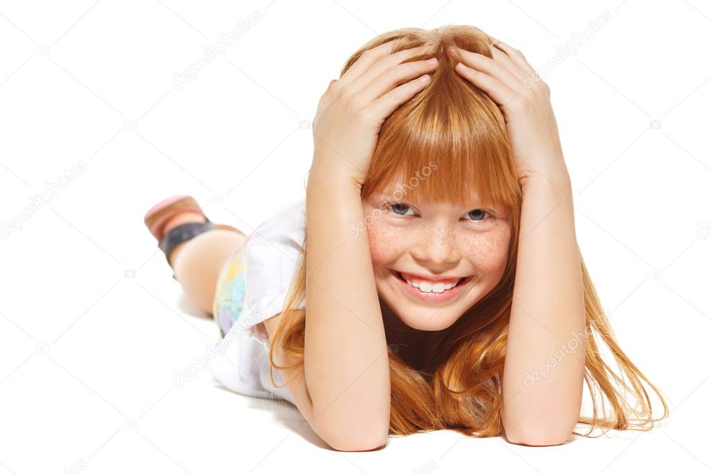 A cheerful little girl with red hair is lying, isolated on the white background