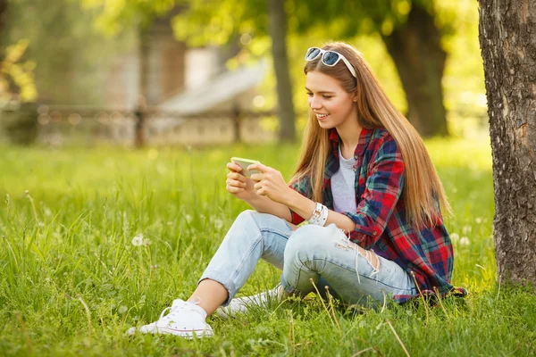 Attractive smiling girl typing on cell phone in summer city park. Modern happy woman with a smartphone, outdoor — Stock Photo, Image