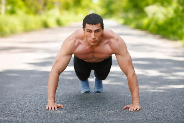 Hombre de fitness ejercitando flexiones, al aire libre. Entrenamiento muscular masculino en el parque de la ciudad — Foto de Stock