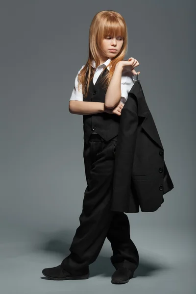 Volledige lengte beetje schattig meisje in zwart pak, met een jas in zijn handen, geïsoleerd over grijze achtergrond — Stockfoto