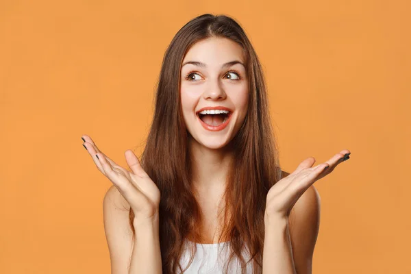 Surprised happy beautiful woman looking sideways in excitement. Isolated on orange — Stock Photo, Image