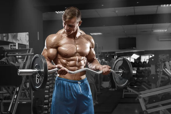 Hombre musculoso ejercitándose en el gimnasio haciendo ejercicios con barra en bíceps, fuertes abdominales masculinos desnudos del torso —  Fotos de Stock