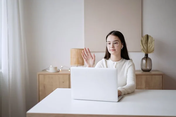 Cute teenage girl waving hand with online teacher on laptop screen at home. Education concept, distance learning, self-education, video conference class with tutor