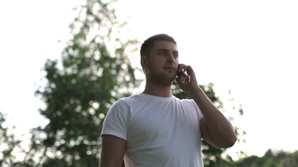 Człowiek w okulary na zewnątrz rozmawia przez telefon na zachód zwolnionym tempie — Wideo stockowe