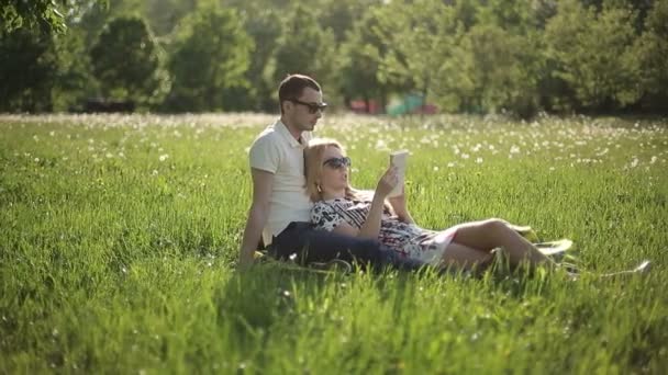 Loving couple in sunglasses at sunset read book on field with dandelions — Stock Video