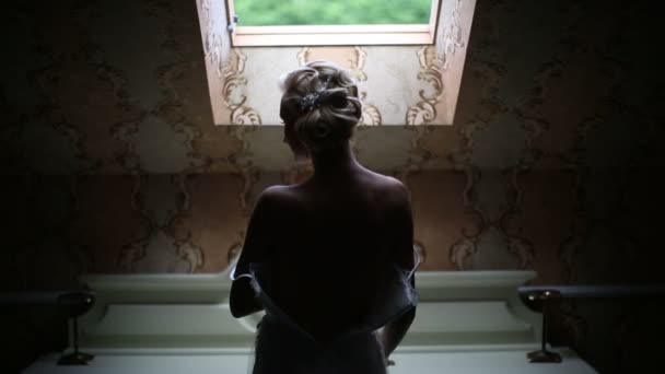 Elegante novia caucásica lleva un vestido de novia de pie en la ventana — Vídeo de stock