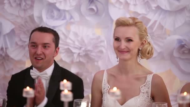 Recién casados sentados en una mesa en su boda aplaudiendo y sonriendo de cerca — Vídeo de stock