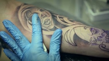 Dövme sanatçısı çalışma. Adam kolunu kadının yüzünde çizer. Dövme salonu