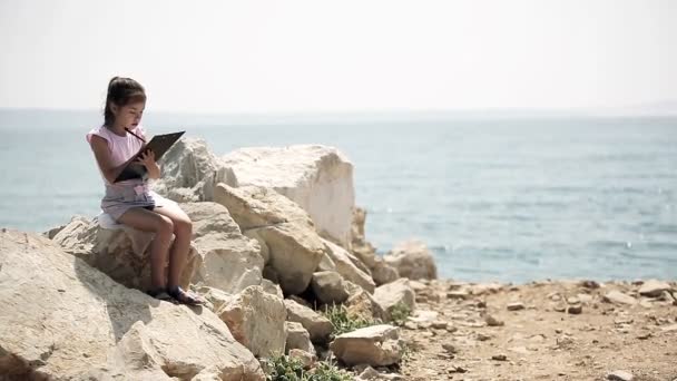 Un bambino siede su una pietra vicino al mare Adriatico e disegna un disegno . — Video Stock